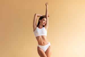 Woman in white underwear and sports bra showing slim body from CoolSculpting in Calgary, AB