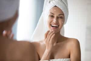 Woman in a towel smiling applying moisturizer after a MicroLaser Peel in Calgary